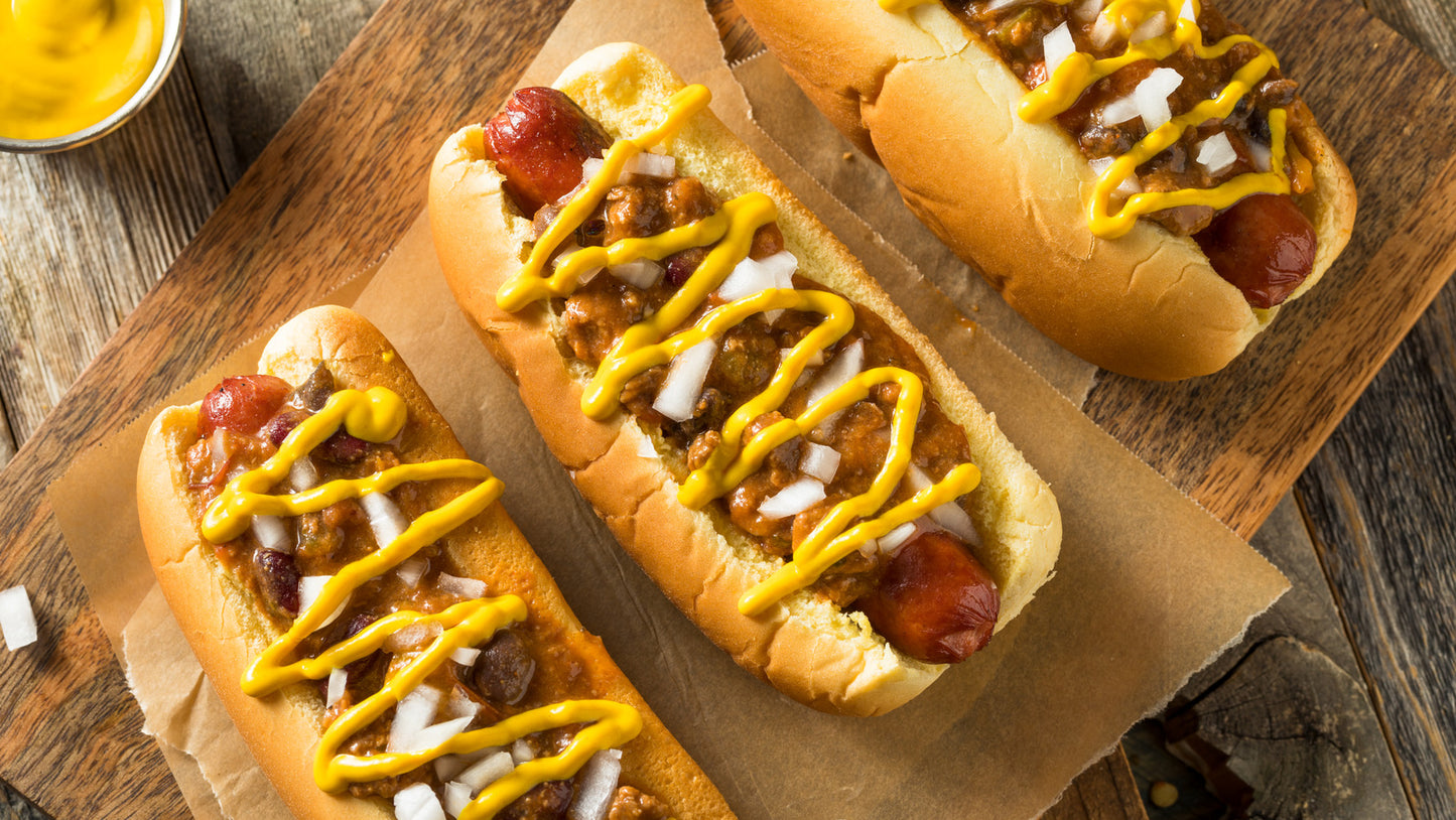 hotdogs in buns covered in chili, mustard and onions
