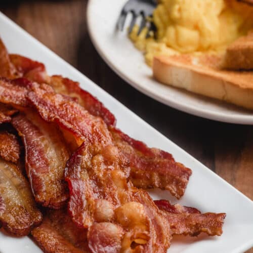 A plate of cooked, Uncured bacon with a side of eggs and toast.